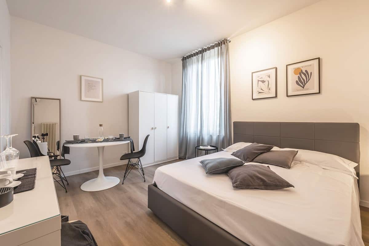 A modern hotel room with a bed, desk, chair, and wardrobe.