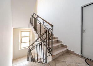 Una escalera con barandilla de hierro forjado, una puerta con mirilla y un ventanal que deja entrar luz natural.