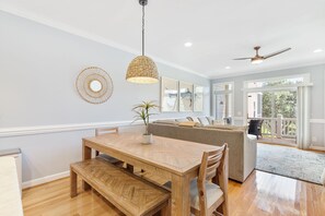 Ein Essbereich mit Holztisch und Bänken, einer hängenden Lampe und einer Couch im Hintergrund.