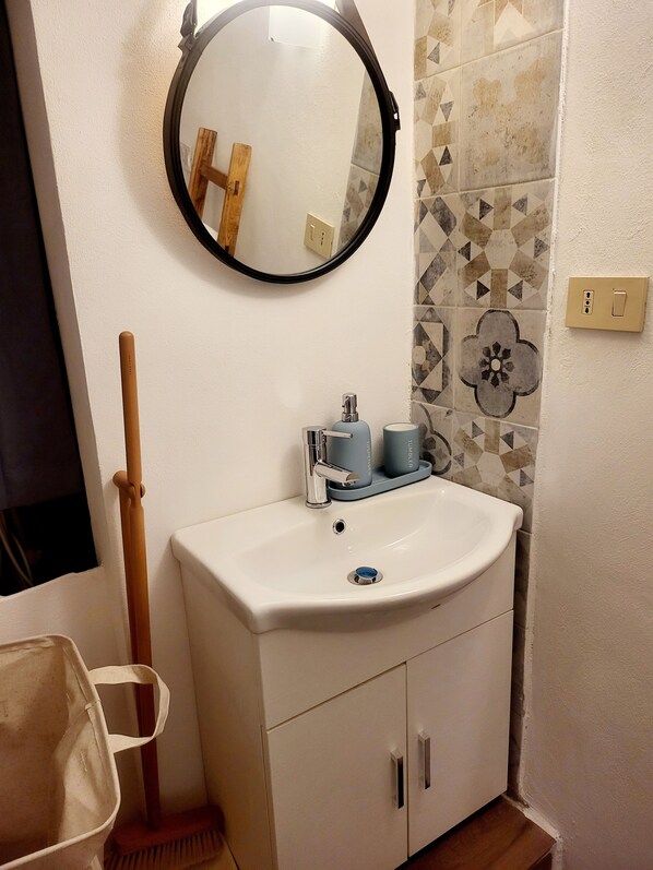 A bathroom with a white sink, a mirror, and a toilet. There is a broom and a dustpan on the floor.