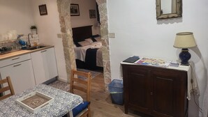 A compact room with a kitchenette, a bed, a dining area, and a small table with a lamp. - Il Rifugio (Palermo)