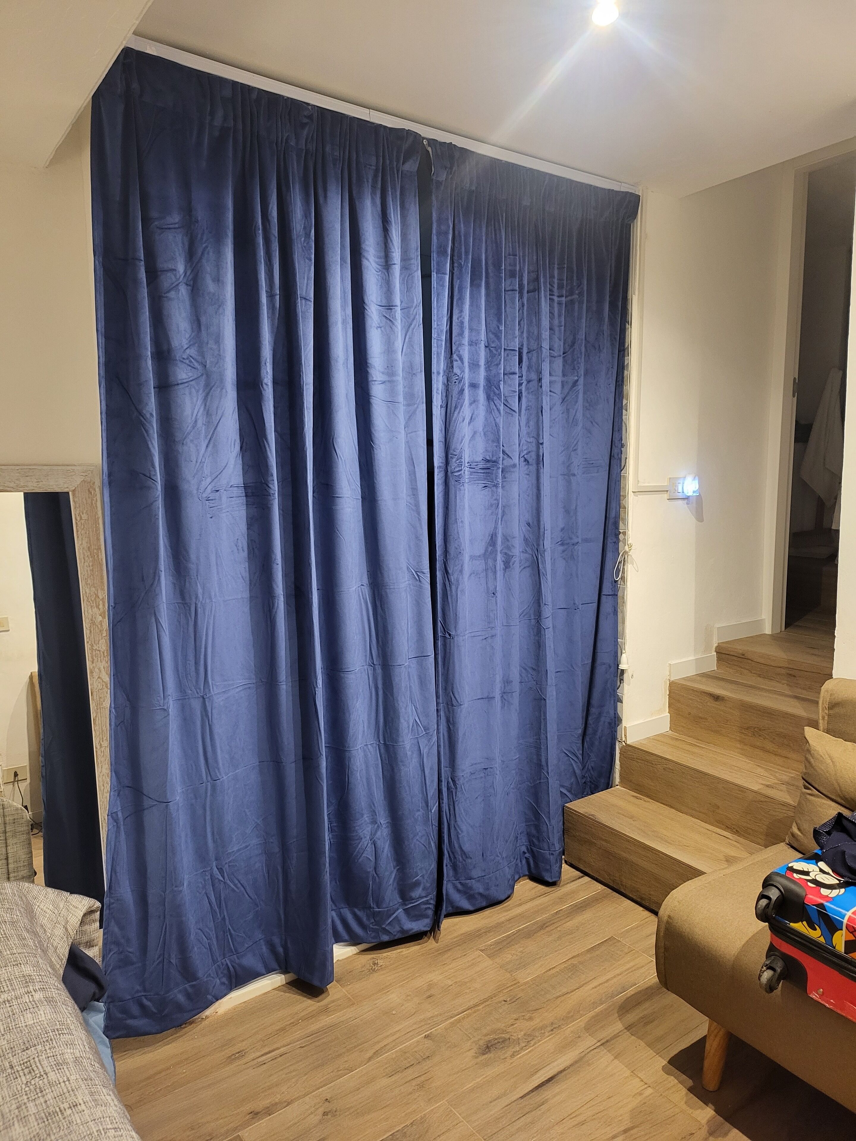 Une pièce dotée d’un grand rideau bleu, d’un plancher en bois et d’un escalier menant à un autre niveau.