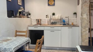 A compact kitchen with white cabinets, a wooden dining table, and a blue chair. - Il Rifugio (Palermo)