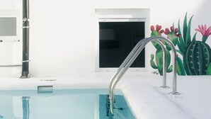 Piscina com escada de metal, parede branca e um mural de cactos.