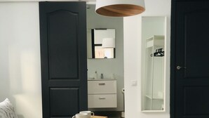 Quarto com cama, mesa de cabeceira com chávenas, espelho, guarda-roupa e porta.