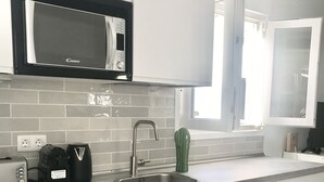 Cozinha moderna com armários brancos, micro-ondas embutido, pia de aço inoxidável e janela que proporciona iluminação natural.