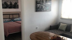 Un espacio habitable compacto con cama, sofá, mesa de comedor y un cuadro de la ciudad en la pared.