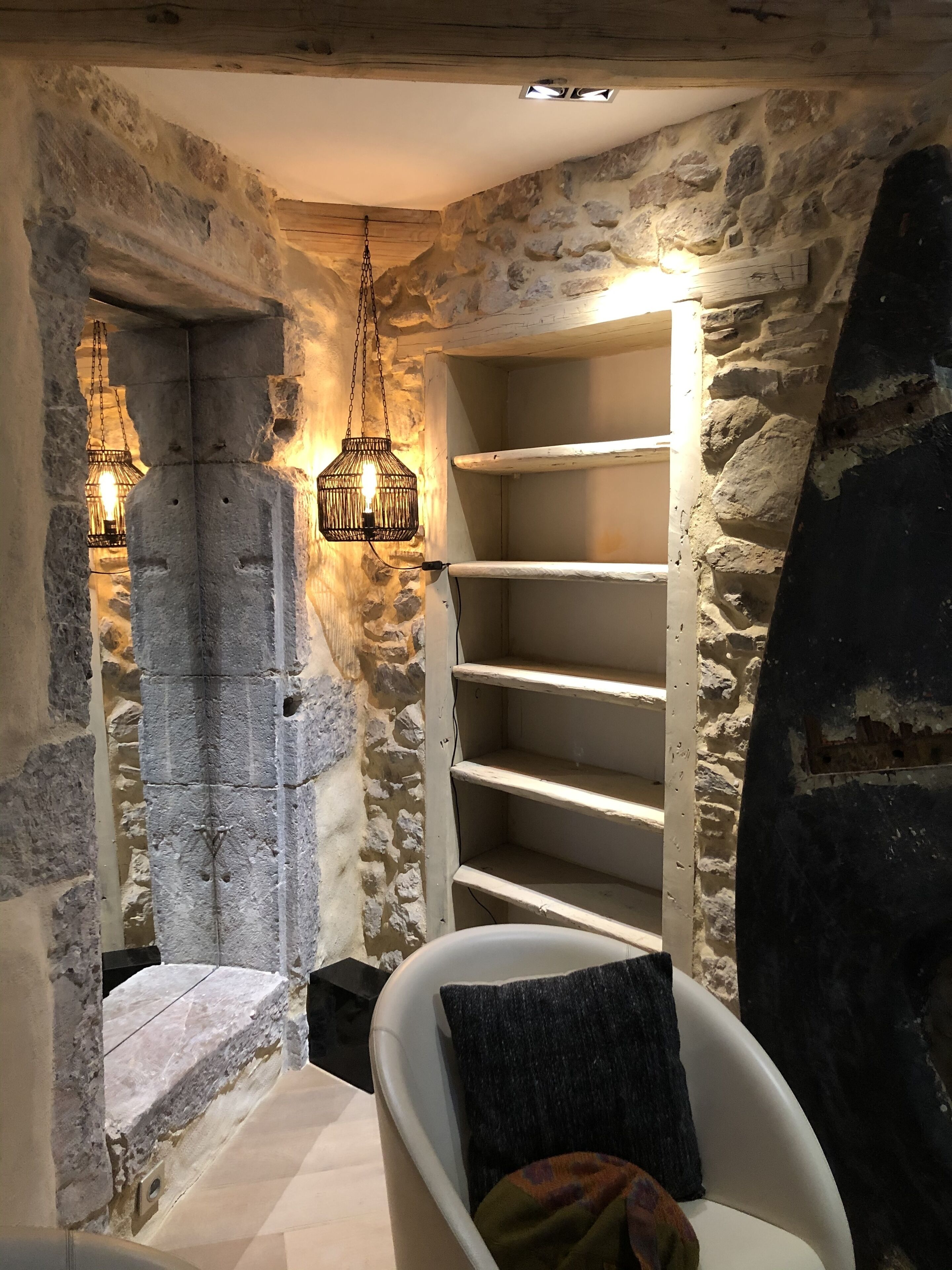 A stone-walled room with a bathtub, a wooden staircase, and hanging light fixtures.