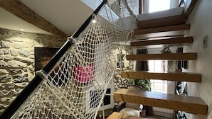 A multi-level interior with a netted play area, wooden beams, stone walls, and a staircase. - Cozy duplex apartment on the quays of Sète (Sète)
