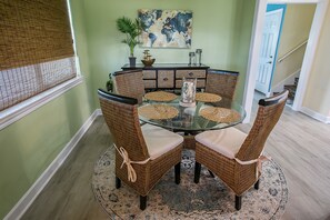 Un coin repas avec une table ronde en verre entourée de chaises en osier dotées d’assises rembourrées, un élément décoratif central et un grand tableau abstrait accroché au mur.