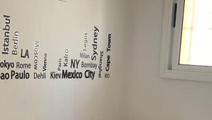 Une chambre d’hôtel avec un lit, des oreillers et un mur sur lequel sont écrits des noms de villes.