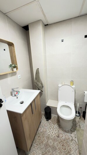 Een badkamer met een witte wastafel, houten kastje, toilet en vloertegels met een patroon.