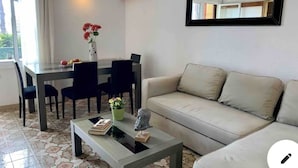 Un salon comprenant un canapé, une table basse, une table à manger avec des chaises, une plante en pot et un miroir fixé au mur.