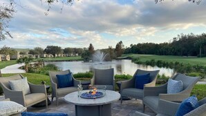 A patio with wicker furniture, a round table with a fire pit, and a view of a golf course and pond.