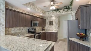 A kitchen with granite countertops, dark wooden cabinets, a microwave, stove, and a refrigerator.