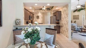 A modern kitchen with stone backsplash, wooden cabinets, and a dining area with wicker chairs and a glass table.