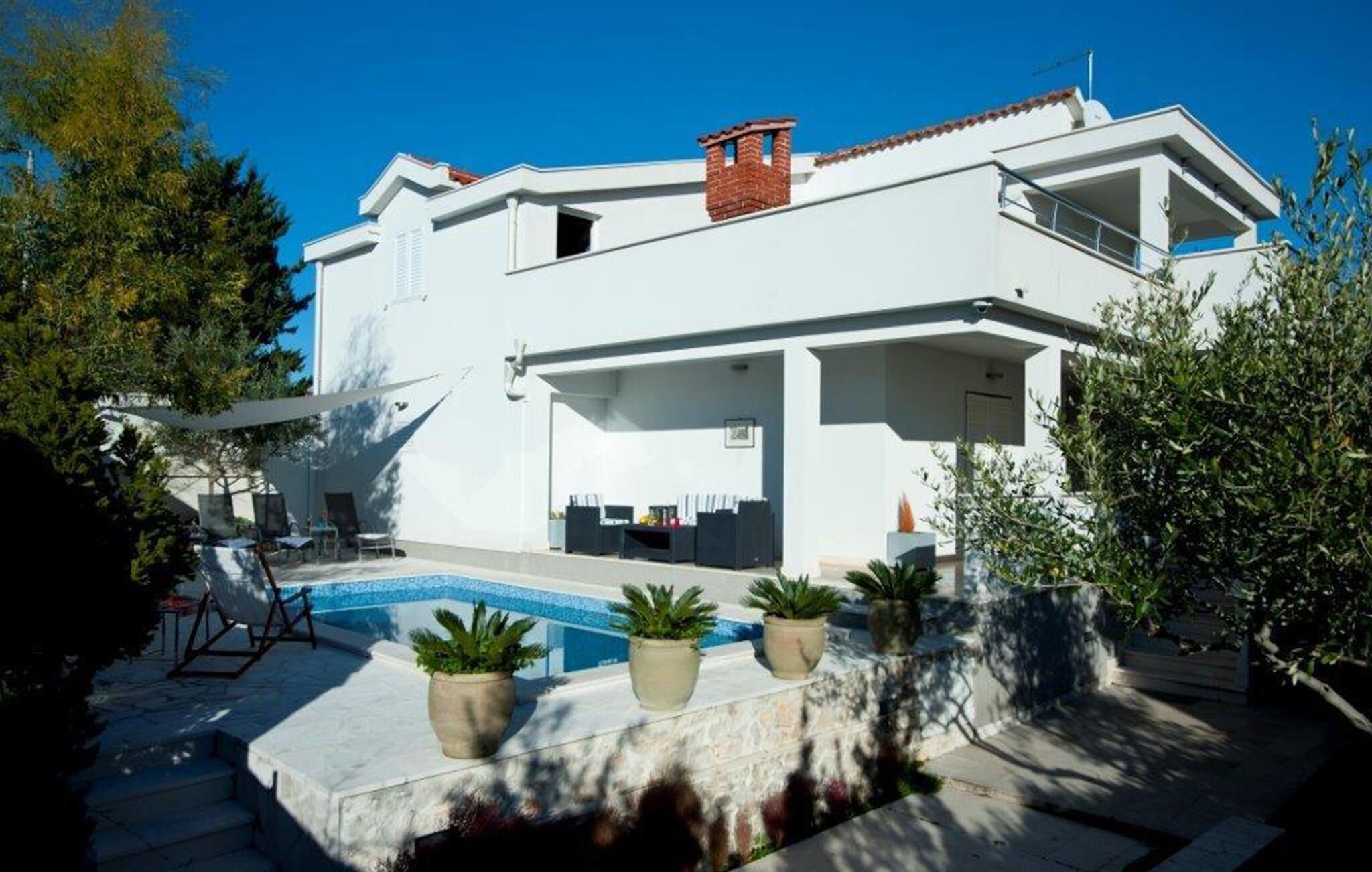 Een moderne witte villa met een zwembad, buitenzitplaatsen en potplanten.