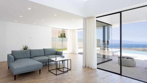 A modern living room with a sectional sofa, a coffee table, and a view of a pool and mountains through large glass doors. - "New Home Costa Adeje, Luxurious Private Villa" (Costa Adeje)