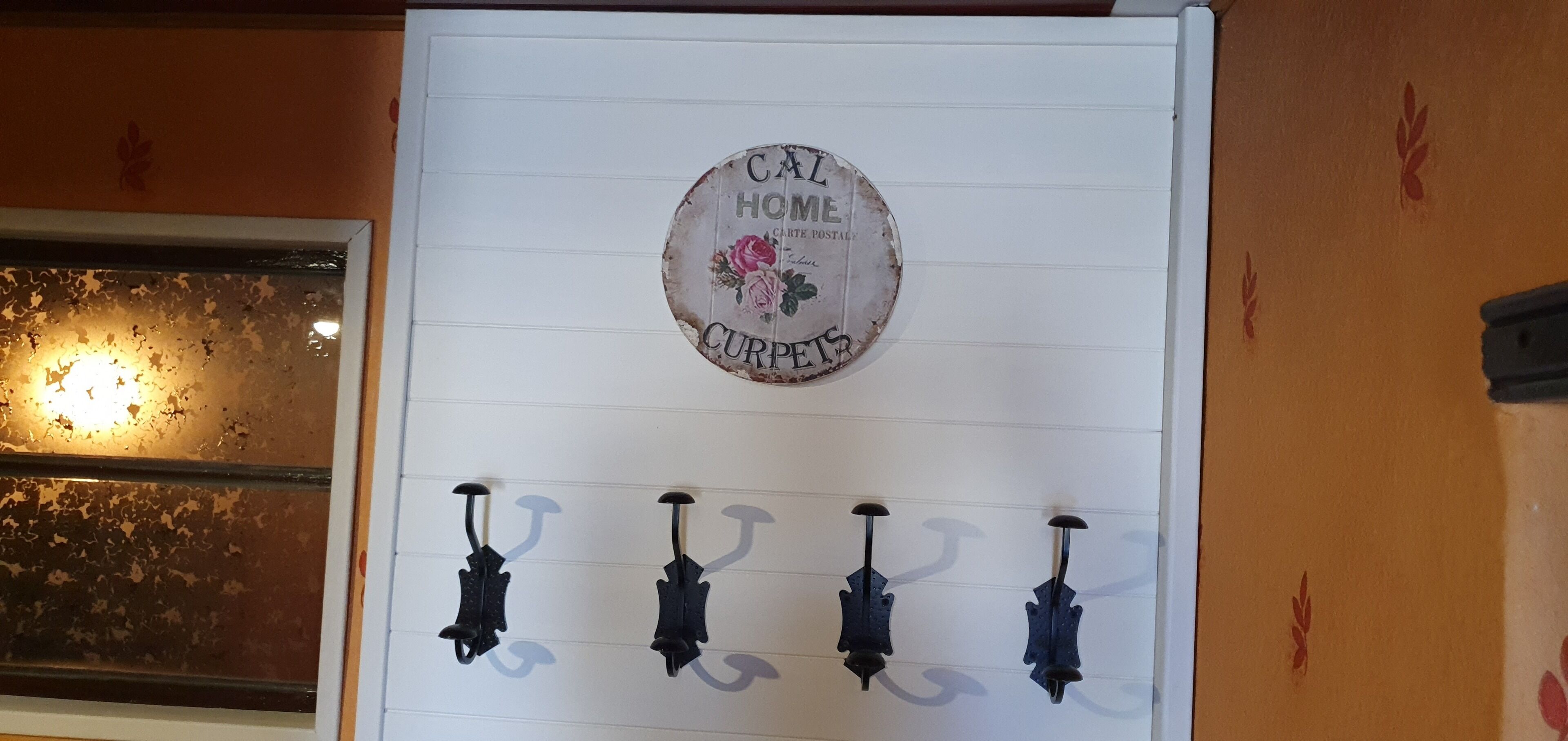 Una pared con un letrero circular que dice "CAL HOME CURPETS" y cuatro ganchos negros debajo.