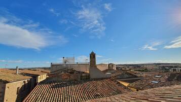 Una vista panoramica di una città storica con tetti in tegole di terracotta, un’imponente torre campanaria e un cielo azzurro intenso.