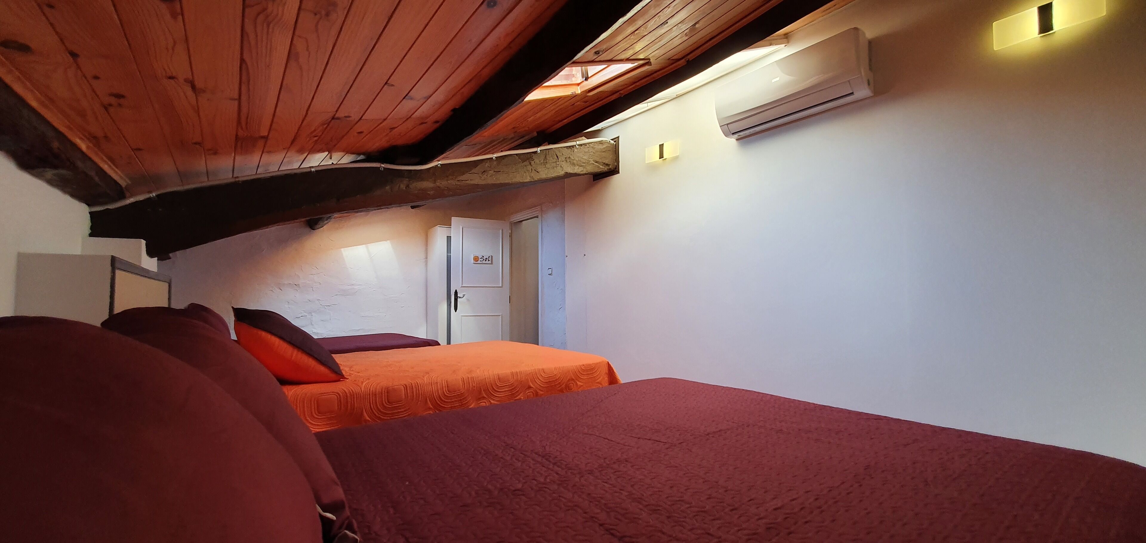 A room with two beds, wooden ceiling beams, an air conditioning unit, and a small window.