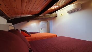 A room with two beds, wooden ceiling beams, an air conditioning unit, and a small window.