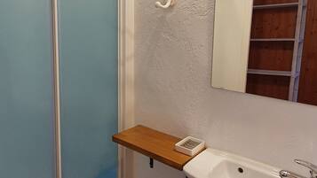 Un baño con un lavamanos blanco, un estante de madera, un espejo y una zona de ducha.