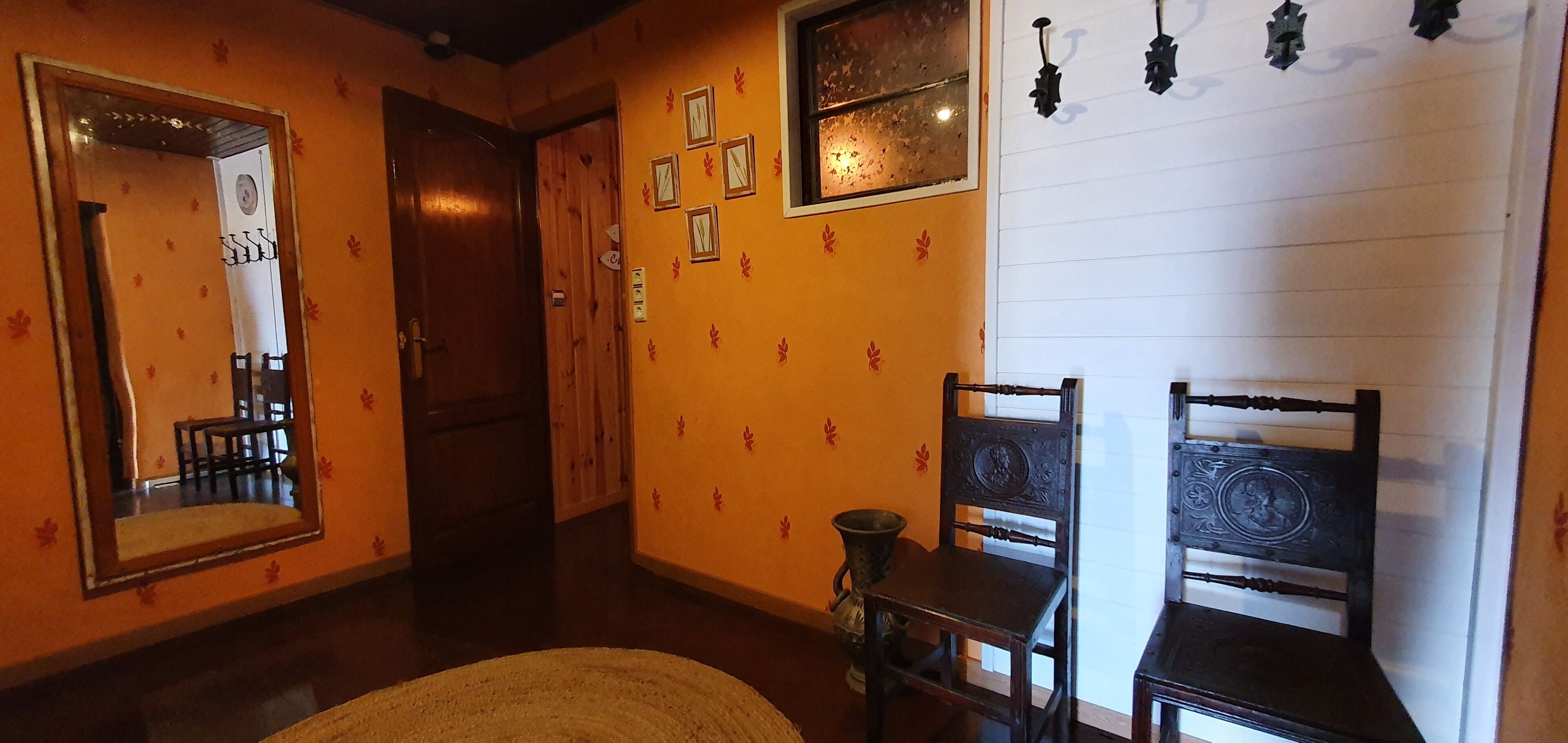 Un pasillo con una puerta de madera, un espejo y una silla.
