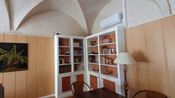 A room with wooden panel walls, a white bookshelf, a table with chairs, and a ceiling with arched designs.