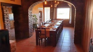 A long dining table with chairs, set in a room with brick walls and a tiled floor.