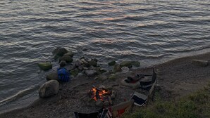 Eine Strandansicht mit Lagerfeuer, Felsen und einem Sonnenuntergang über dem Wasser.