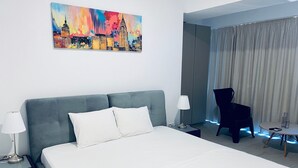Ein Hotelzimmer mit Bett, Stuhl, Lampe, einem Gemälde und Blick auf die Stadt.