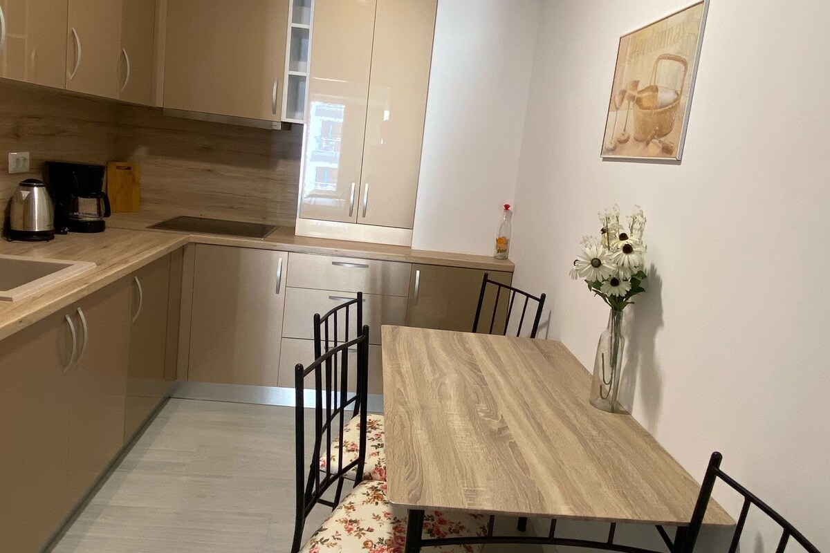 A modern kitchen with a dining table, chairs, and a vase of flowers.