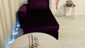 Ein modernes Zimmer mit einem violetten Sofa, einem runden Tisch mit Kerzenhalter und zwei Bildern an der Wand.