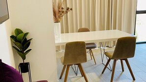 Ein modernes Wohnzimmer mit einem violetten Sofa, einem Esstisch mit Stühlen, einer Zimmerpflanze und einem großen Fenster mit Vorhängen.