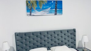 A bed with a tufted headboard, white bedding, two bedside lamps, and a framed picture of a beach scene. - Maritimo 6C (Constanta)