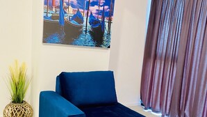 A modern living room with a blue sofa, a painting of a cityscape, a potted plant, and a window with curtains. - Maritimo 6C (Constanta)