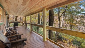 A wooden deck with benches and a grill, overlooking a forested area. - Timber Lodge - Private, Serene Cabin with Game Room for Kids (Todd)