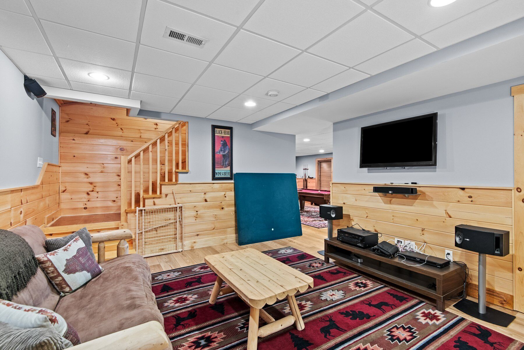 A modern living room with a wooden staircase, a flat-screen TV, a pool table, and a cozy seating area.