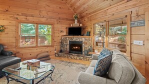 A cozy cabin interior with a stone fireplace, wooden walls, a leather sofa, and a glass coffee table. - Timber Lodge - Private, Serene Cabin with Game Room for Kids (Todd)
