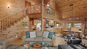 A spacious wooden cabin with a loft bedroom, a cozy living room with a sofa and coffee table, and a kitchen area. - Timber Lodge - Private, Serene Cabin with Game Room for Kids (Todd)