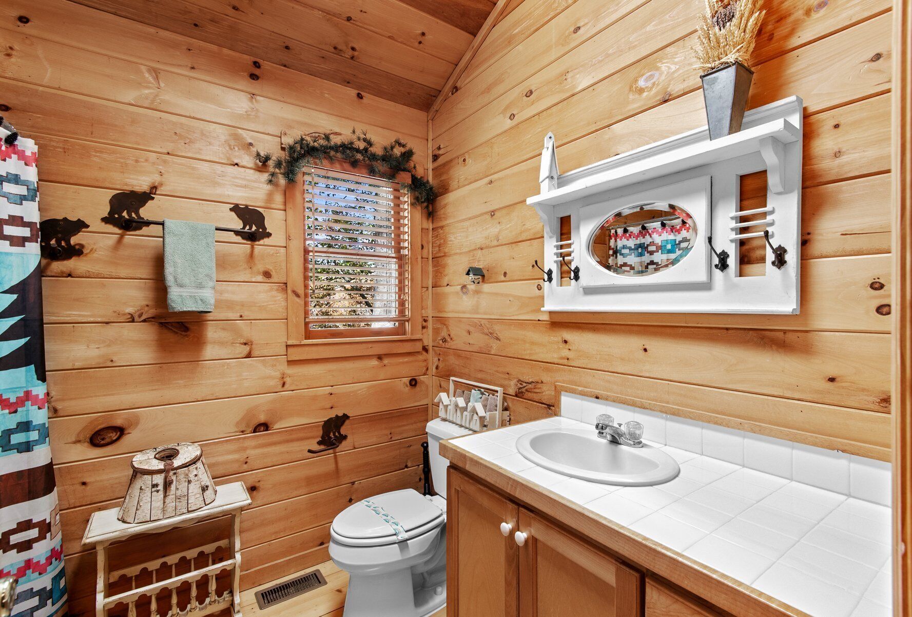 A wooden cabin bathroom with a toilet, sink, and window.