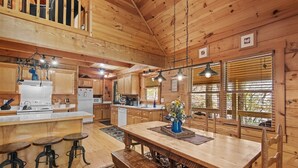 A rustic wooden cabin interior with a kitchen, dining area, and a loft bedroom. - Timber Lodge - Private, Serene Cabin with Game Room for Kids (Todd)