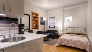 A compact bedroom with a bed, bedside table, and a small window. - Downtown Retreat: Stylish Boston Studio (Boston)