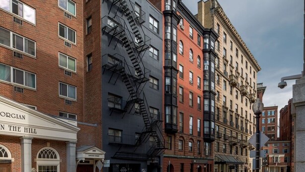 A multi-story building with a fire escape, a sign reading "ORGIAN IN THE HILL," and parked cars on the street. - Downtown Retreat: Stylish Boston Studio (Boston)