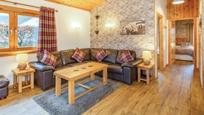 A cozy living room with a stone wall, wooden ceiling, and a large window with curtains. - 2 bedroom accommodation in Torlundy, near Fort William (Torlundy, near Fort William)