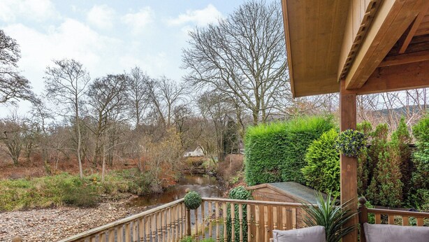 A wooden deck with wicker furniture and a view of a river and trees. - 2 bedroom accommodation in Torlundy, near Fort William (Torlundy, near Fort William)