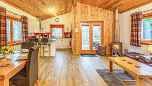 A cozy cabin interior with a wooden ceiling, a dining area with a table and chairs, a kitchen with a stove, and a living area with a sofa and fireplace. - 2 bedroom accommodation in Torlundy, near Fort William (Torlundy, near Fort William)