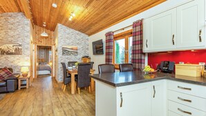 A cozy interior with a wooden ceiling, stone walls, a dining area with a table and chairs, and a kitchen with white cabinets and a red accent wall. - 2 bedroom accommodation in Torlundy, near Fort William (Torlundy, near Fort William)