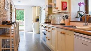 A modern kitchen with white cabinets, a built-in oven, and a sink. There is a dining area with wooden chairs and a table. - 2 bedroom accommodation in Lovington, near Somerton (Lovington, near Somerton)